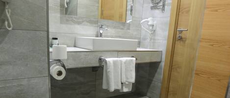 A modern bathroom with a toilet, sink, mirror, and shower.