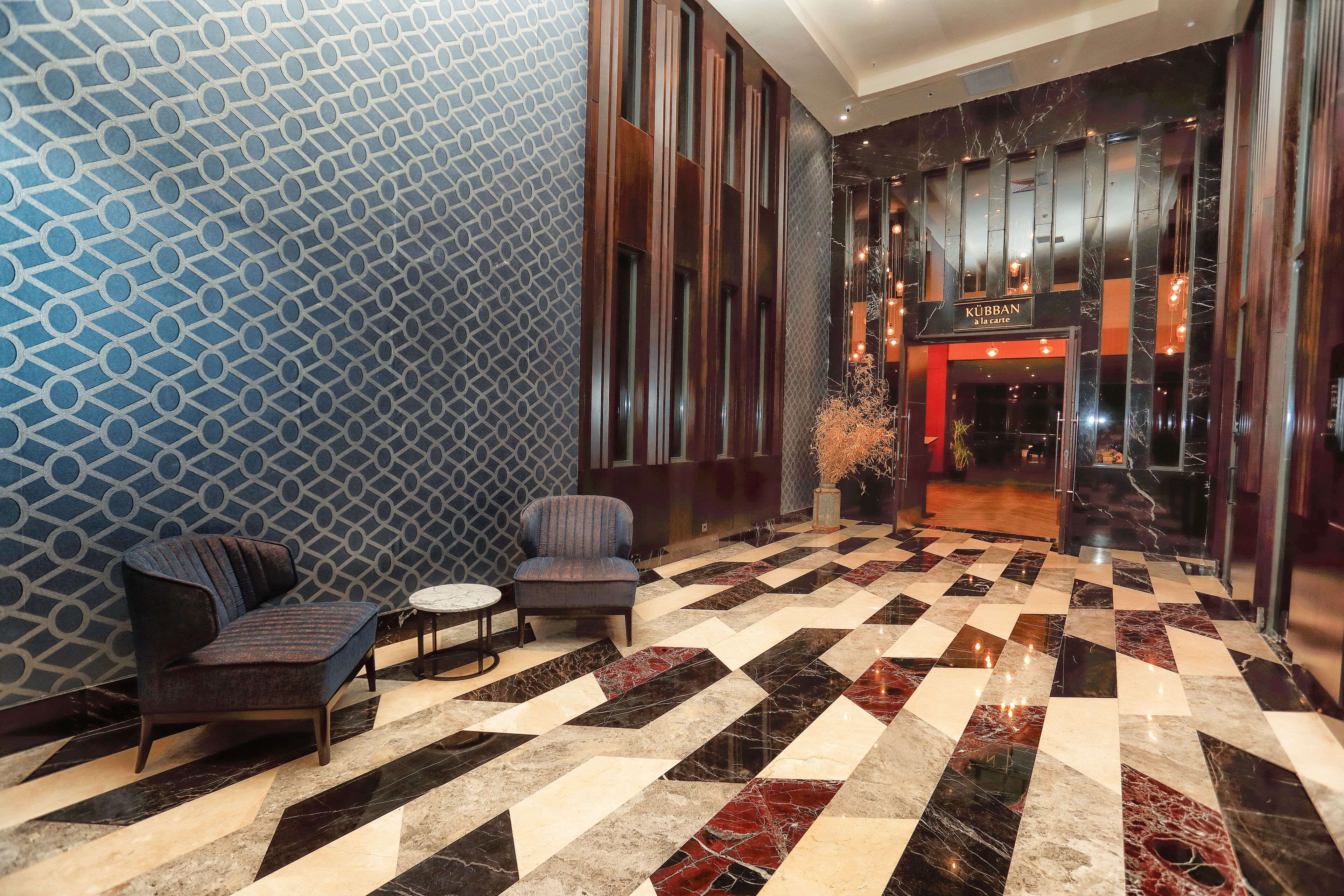 A lobby with a patterned wall, a checkered floor, and a seating area with two sofas and a small table.