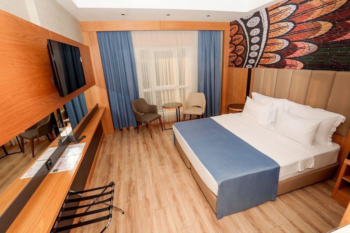 A hotel room with a bed, a desk, a chair, a small table, and a TV.