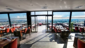 Ein Restaurant mit Panoramablick auf die Stadt, modernem Interieur und roten Stühlen.