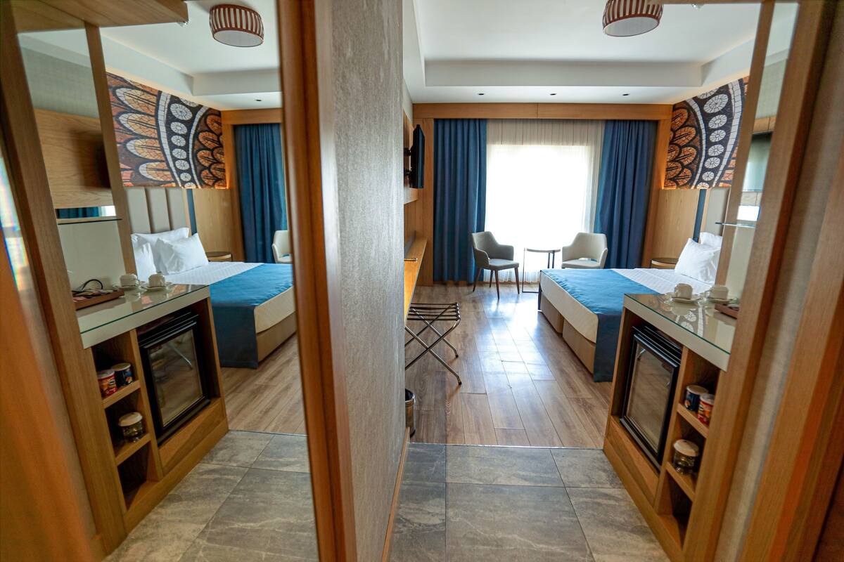 A hotel room with two beds, a small dining area, and a view of the outdoors.