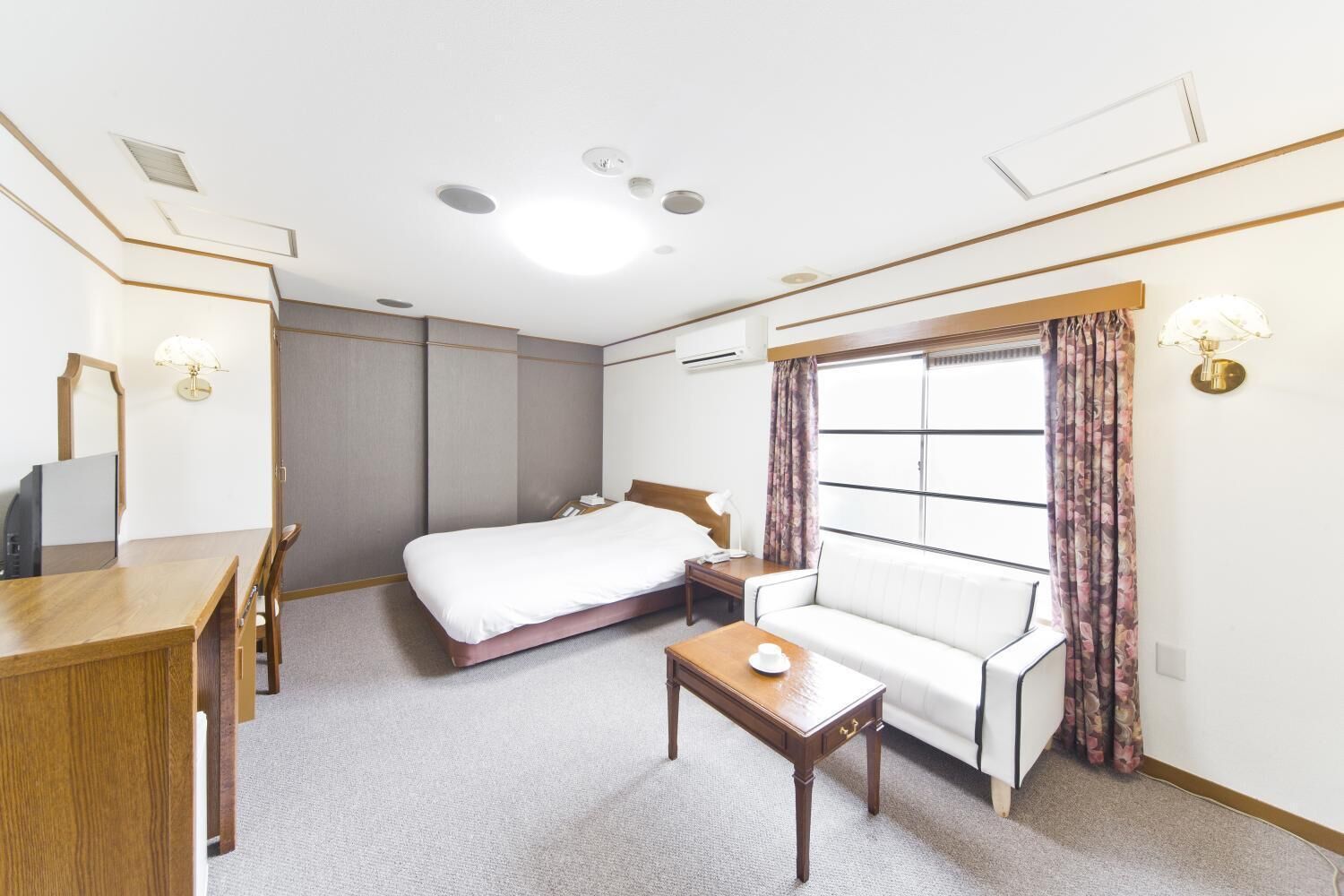 A hotel room with a bed, a sofa, a desk, and a mirror.