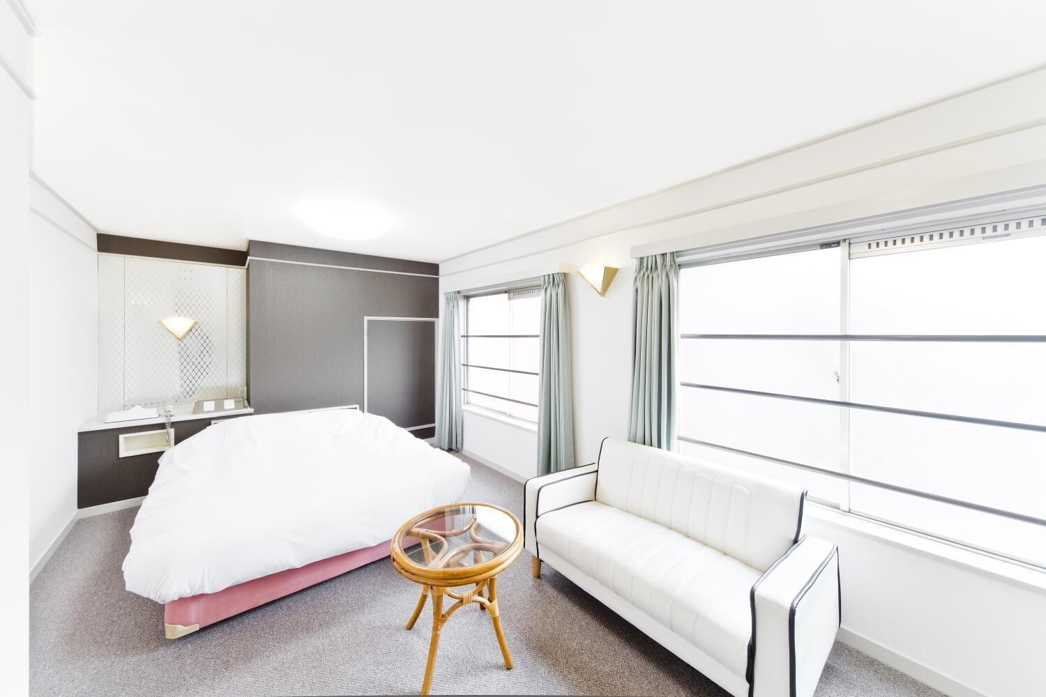A modern hotel room with a large bed, a sofa, a small round table, and a large window with curtains.
