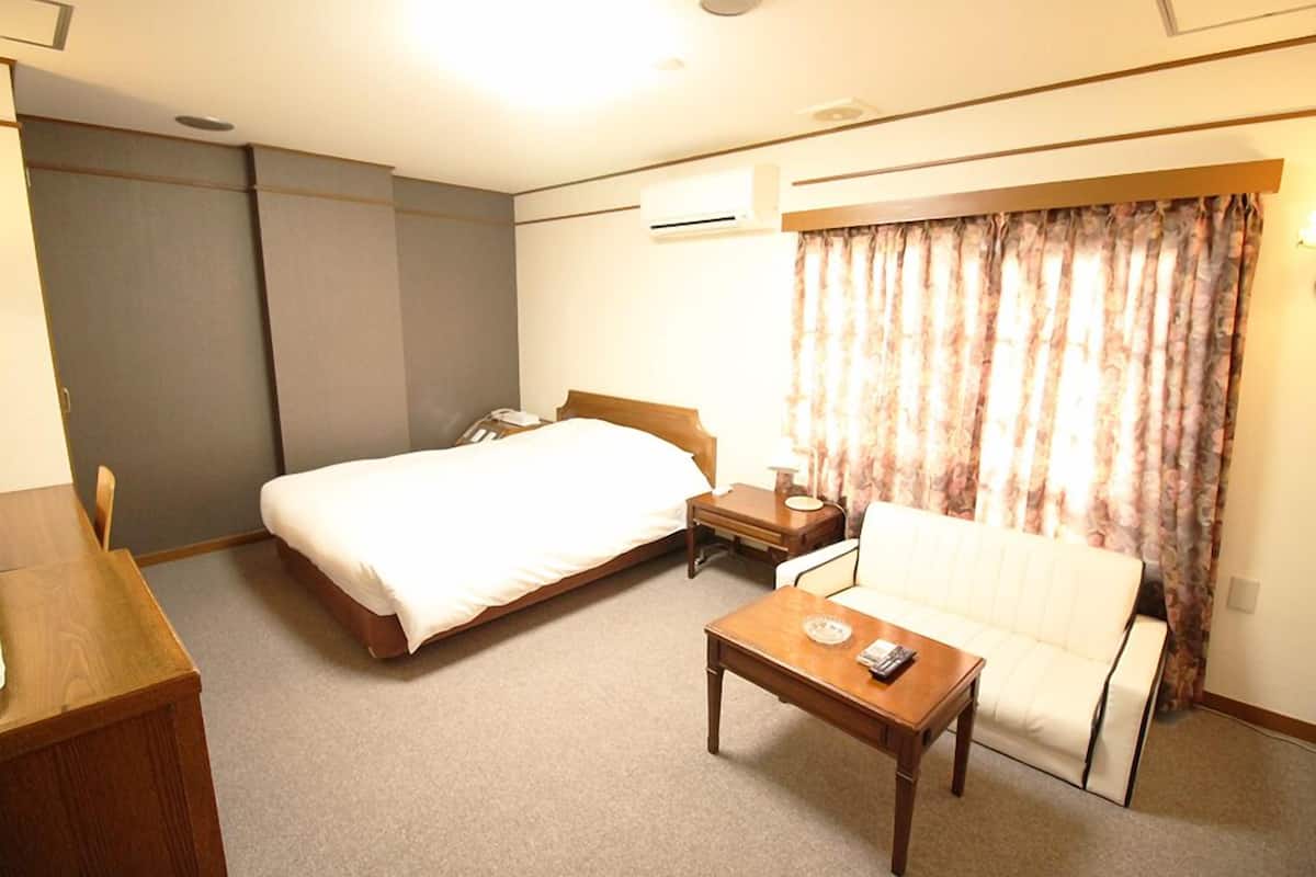 A hotel room with a bed, a sofa, a wooden table, and a curtain.
