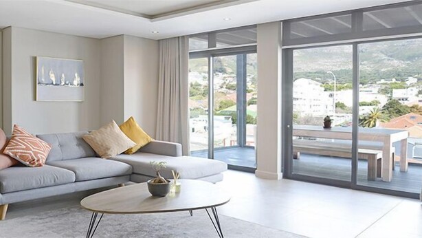 A modern living room with a grey sofa, a round coffee table, and a large window offering a view of the city. - Lily By Stay Amazing (Cape Town)