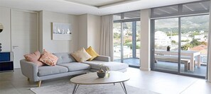 Uma sala de estar moderna com um sofá cinzento, uma mesa de centro redonda e uma grande janela com vista para a cidade.