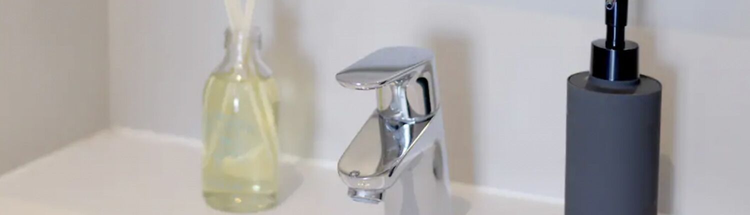 A bathroom with a white sink, a chrome faucet, and a soap dispenser.
