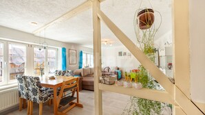 Un vaste espace de vie comprenant une table et des chaises en bois, un canapé et un escalier agrémenté d’une plante suspendue.