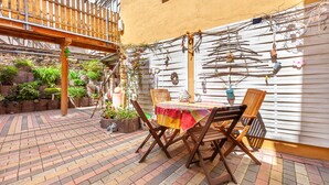 Une terrasse extérieure avec une table et des chaises en bois, entourée de plantes en pot et d’une clôture en bois.