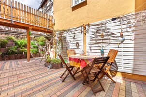 Eine Terrasse im Freien mit einem Holztisch und -stühlen, umgeben von Kübelpflanzen und einem Holzzaun.