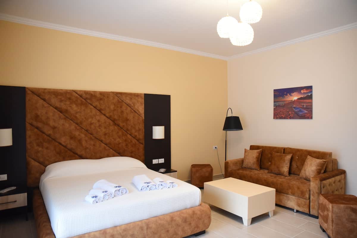 A modern hotel room with a large bed, a sofa, a coffee table, and a painting on the wall.