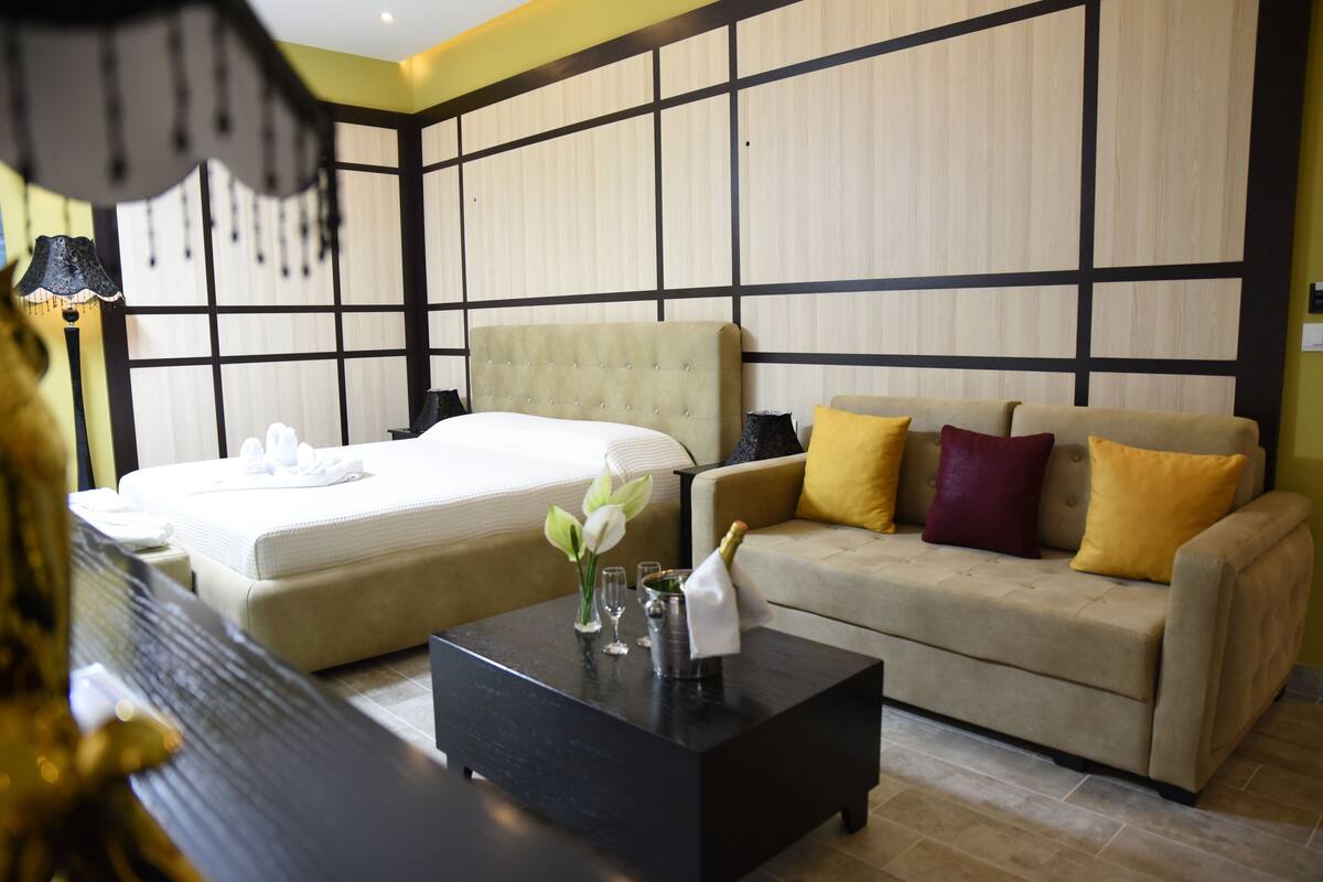 A hotel room with a bed, a sofa, a coffee table, and a decorative vase.