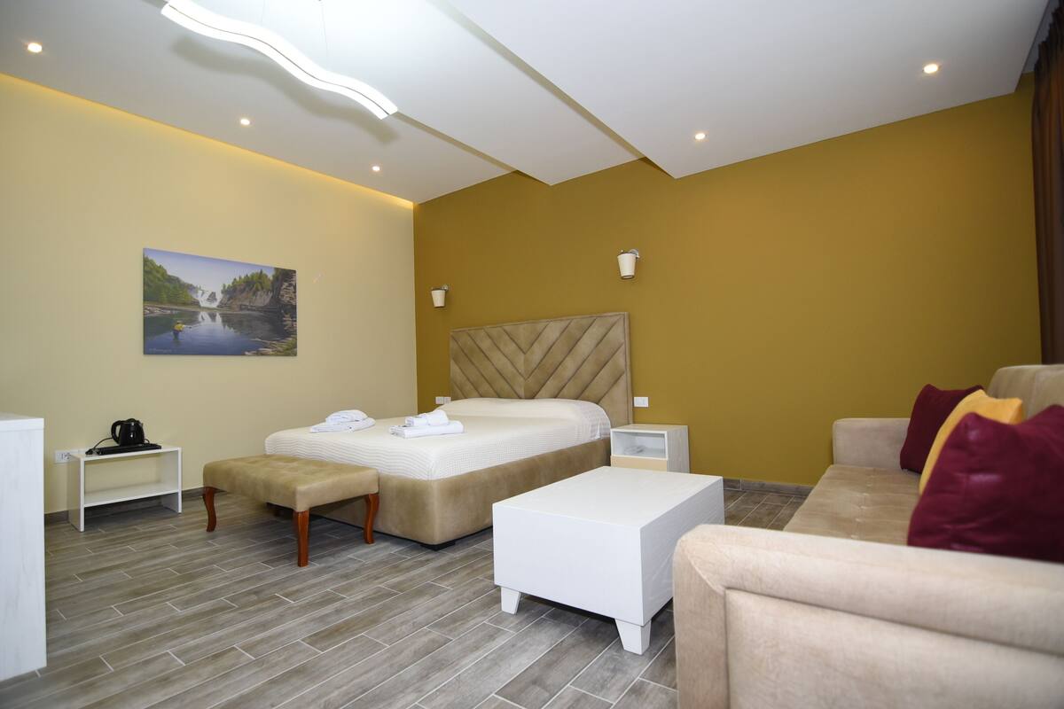 A modern hotel room with a large bed, a sofa, a bench, and a painting on the wall.