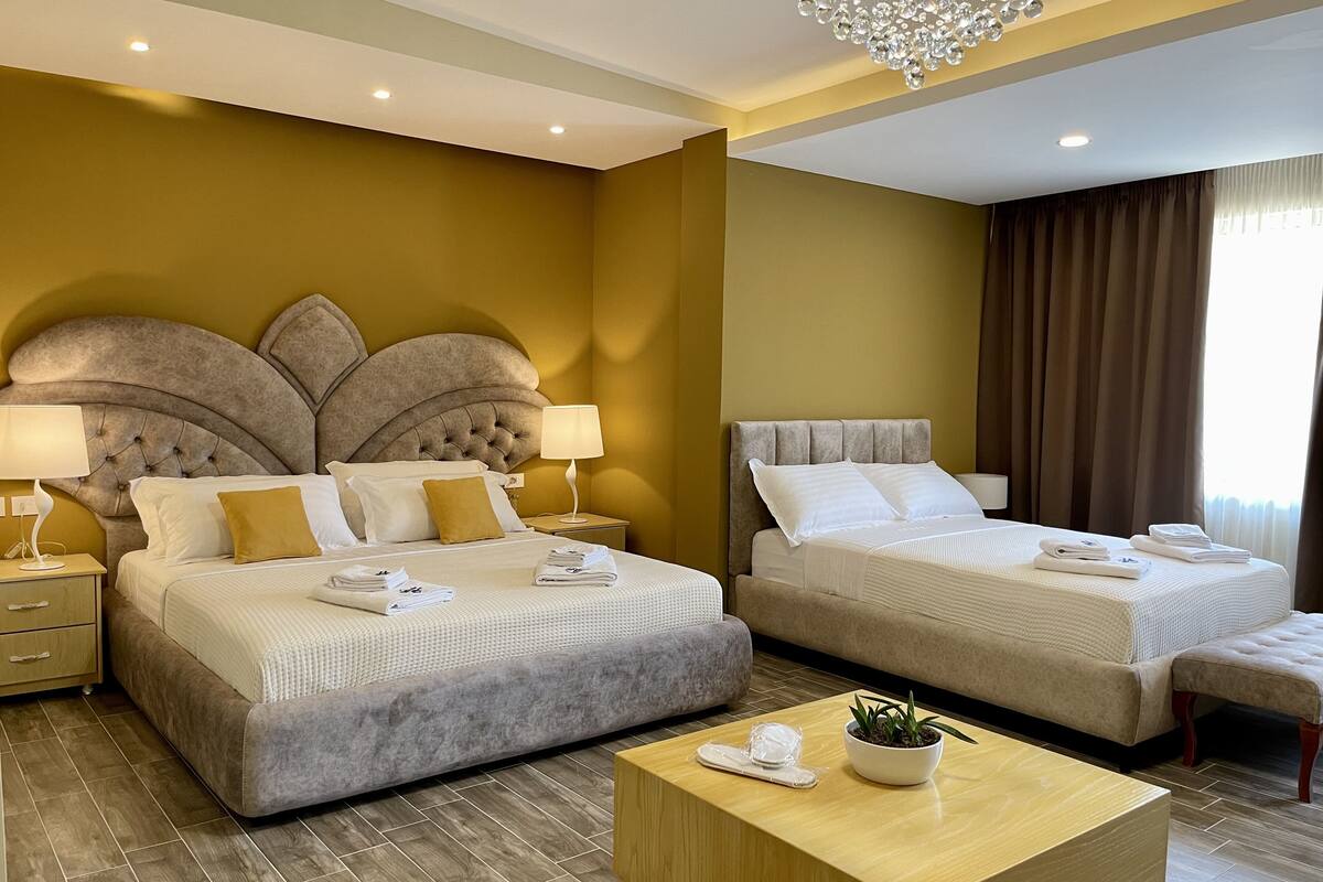 A hotel room with two beds, a wooden coffee table, and a chandelier.