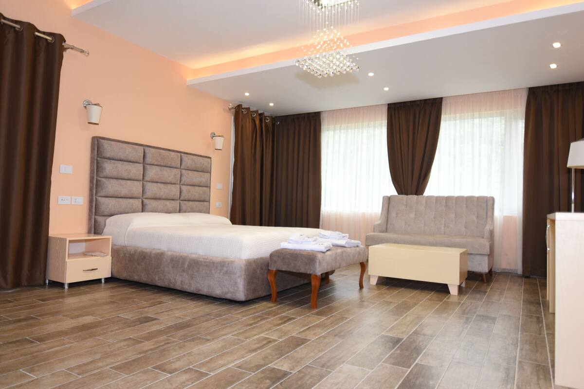 A modern hotel room with a large bed, a sofa, a small table, and a nightstand.