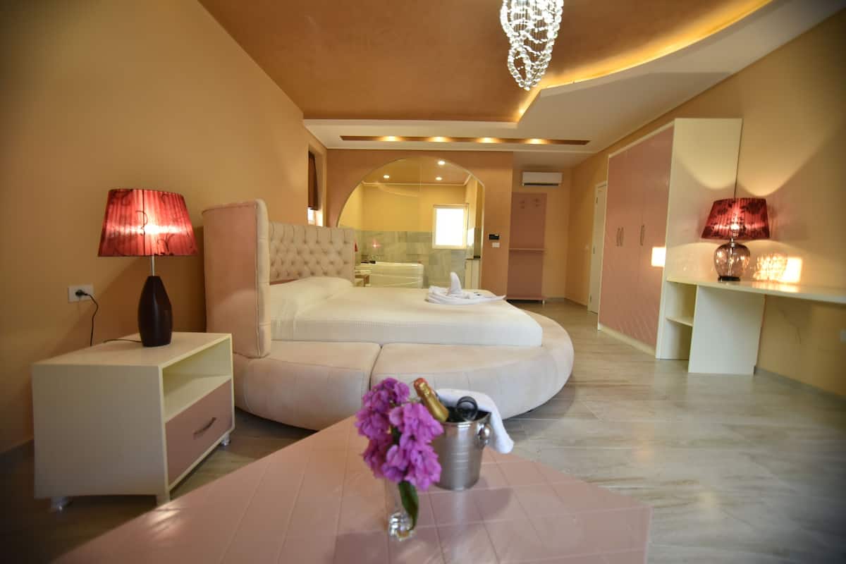 A modern bedroom with a curved bed, bedside lamps, a nightstand, and a vase with flowers.