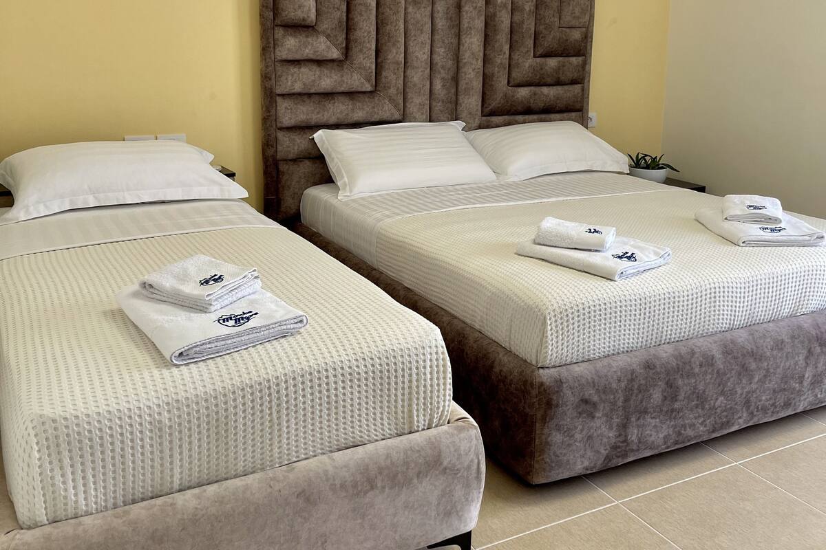 Two beds with headboards, white linens, and folded towels.