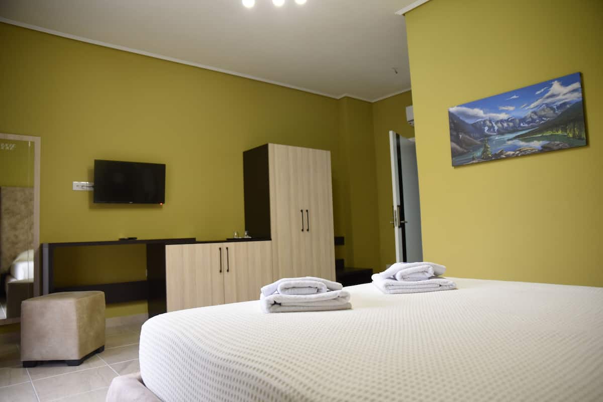 A hotel room with a bed, a television, a painting, and a desk.