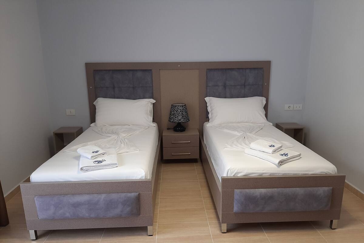 A twin room with two beds, a nightstand with a lamp, and a small table.