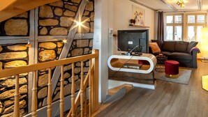 A modern living room with a stone wall, wooden staircase, and a flat-screen TV. - Apartment unter dem Schloss (Quedlinburg)