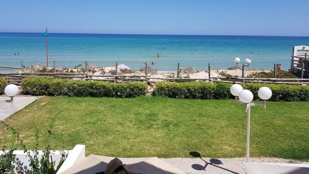 Blick auf die Küste mit blauem Himmel, einem Sandstrand und einer Rasenfläche mit Zaun und Straßenlaternen.