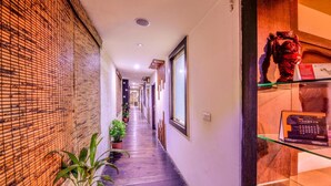 A hallway with a bamboo wall, potted plants, and a glass display case with a calendar. - Raghu Mahal Hotel (Udaipur)