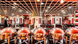 A restaurant interior with a grid ceiling, red and black decor, and multiple tables with clear dome covers. - Raghu Mahal Hotel (Udaipur)