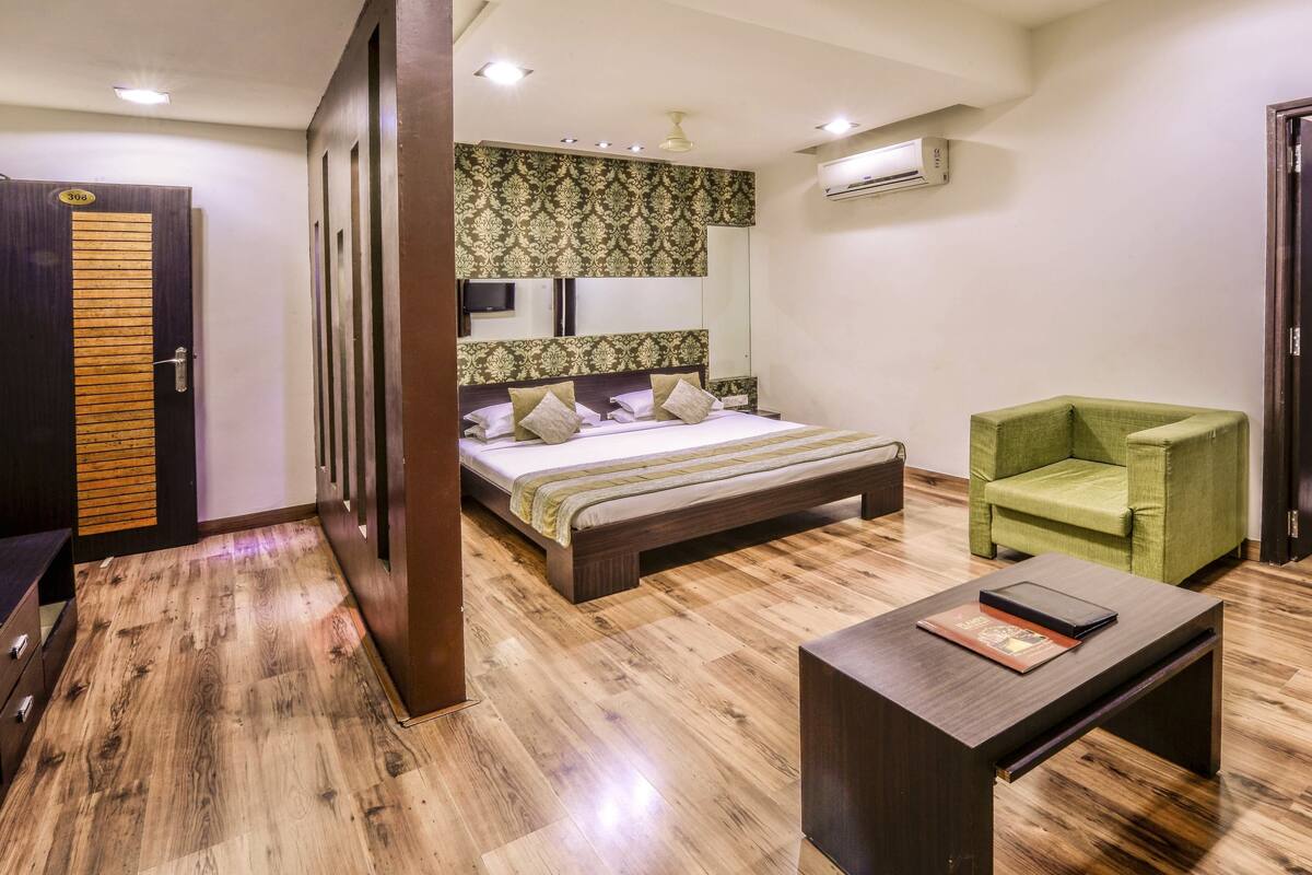 A hotel room with a bed, a green armchair, a wooden coffee table, and a wardrobe.