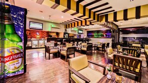 A restaurant with a bar area, wooden furniture, and a large beer advertisement. - Raghu Mahal Hotel (Udaipur)