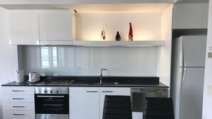 A modern kitchen with white cabinetry, a stainless steel refrigerator, and a glass dining table with two chairs. - Private Apartments at Q1 (Surfers Paradise)