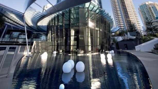 A modern building with a curved glass facade and a reflective pool with spherical decorations. - Private Apartments at Q1 (Surfers Paradise)