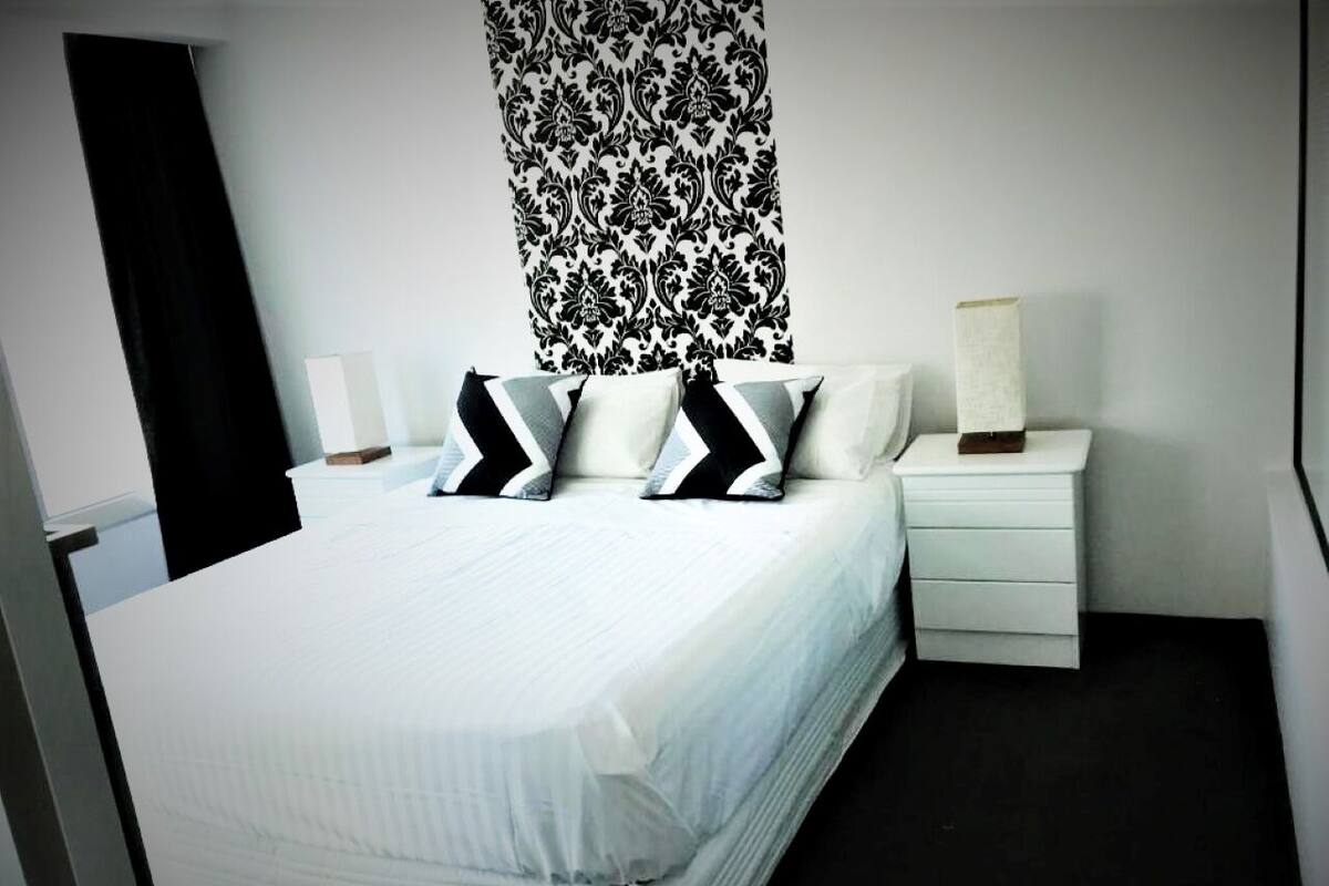 A modern bedroom with a large bed, two bedside tables, and a patterned wall.