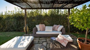 A covered outdoor seating area with a sofa and cushions, a small table, and a potted plant. - Villa Miramare (Camaiore)
