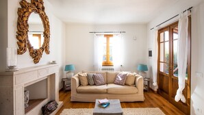 A living room with a beige sofa, a fireplace, a large ornate mirror, and a window with curtains. - Villa Miramare (Camaiore)
