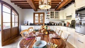 A wooden dining table set with bowls, cups, and plates, surrounded by white chairs in a kitchen with white cabinets and a large window. - Villa Miramare (Camaiore)