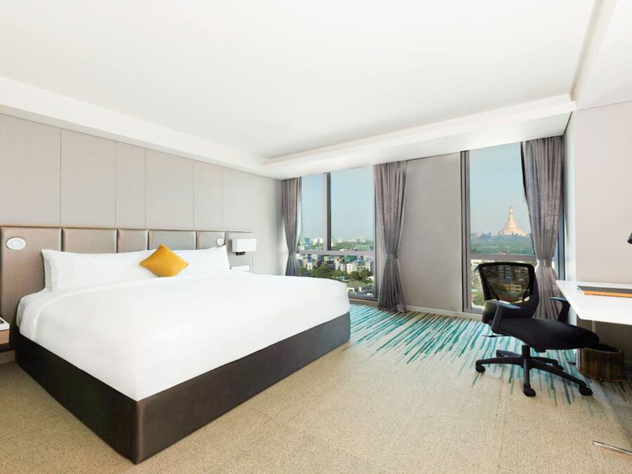 Habitación de hotel con una cama grande, un escritorio y vistas a un paisaje urbano.