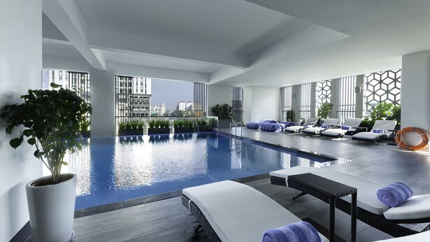 A modern indoor pool area with lounge chairs, a potted plant, and a view of the cityscape. - Zealax Hotel & Residence (Yangon)
