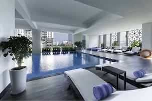 Un área interior de piscina moderna con sillones de descanso, una planta en maceta y vistas a la ciudad.
