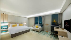 A hotel room with a large bed, a desk, a sofa, a small table with flowers, a TV, and a view of a cityscape at night. - Zealax Hotel & Residence (Yangon)