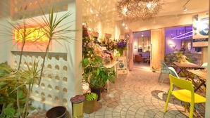 A well-lit indoor space with a tiled floor, potted plants, and a variety of seating arrangements including chairs and tables. - Lestel Naha - Hostel (Naha)
