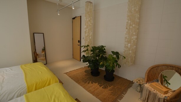 A modern hotel room with a bed, two potted plants, a wicker chair, and a mirror. - Lestel Naha - Hostel (Naha)