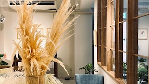 A modern interior with a large window, a blue chair, a round table, and a vase with pampas grass. - Lestel Naha - Hostel (Naha)