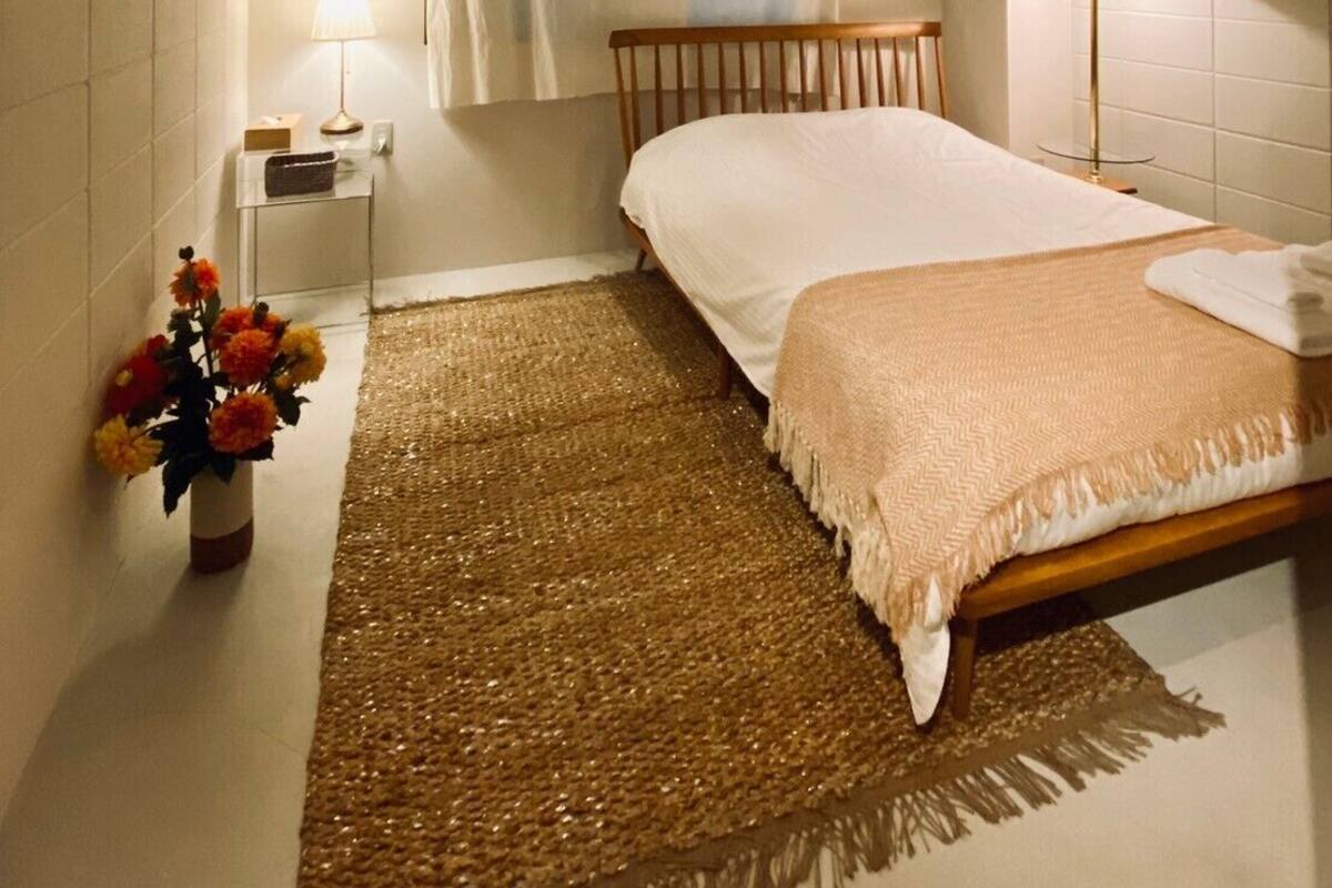 A bedroom with a bed, bedside lamp, air conditioning unit, and a decorative mirror on the wall.