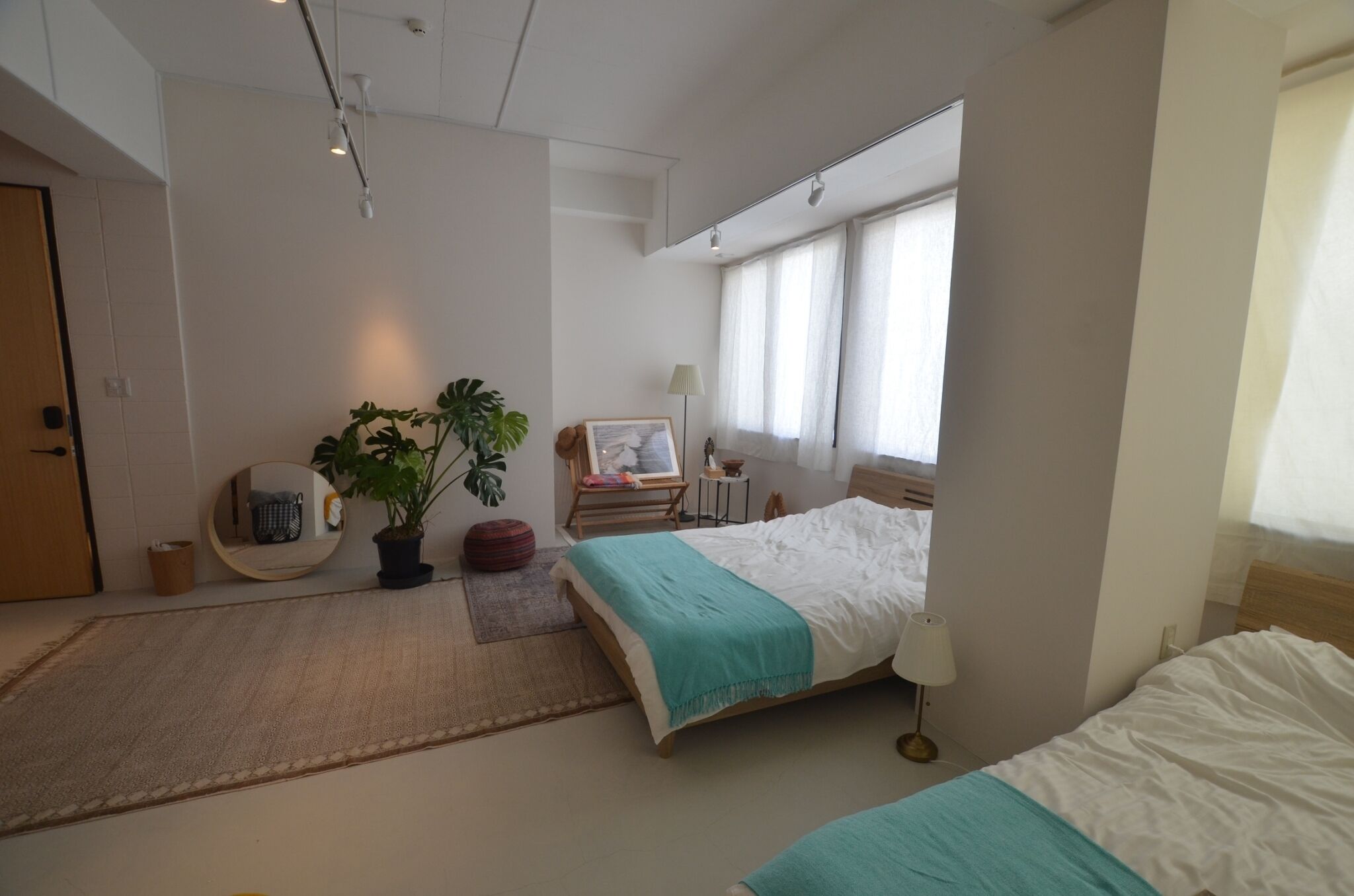 Moderni hotellihuone, jossa on kaksi sänkyä, suuri ikkuna, ruukkukasvi ja pieni pöytä, jossa on lamppu.