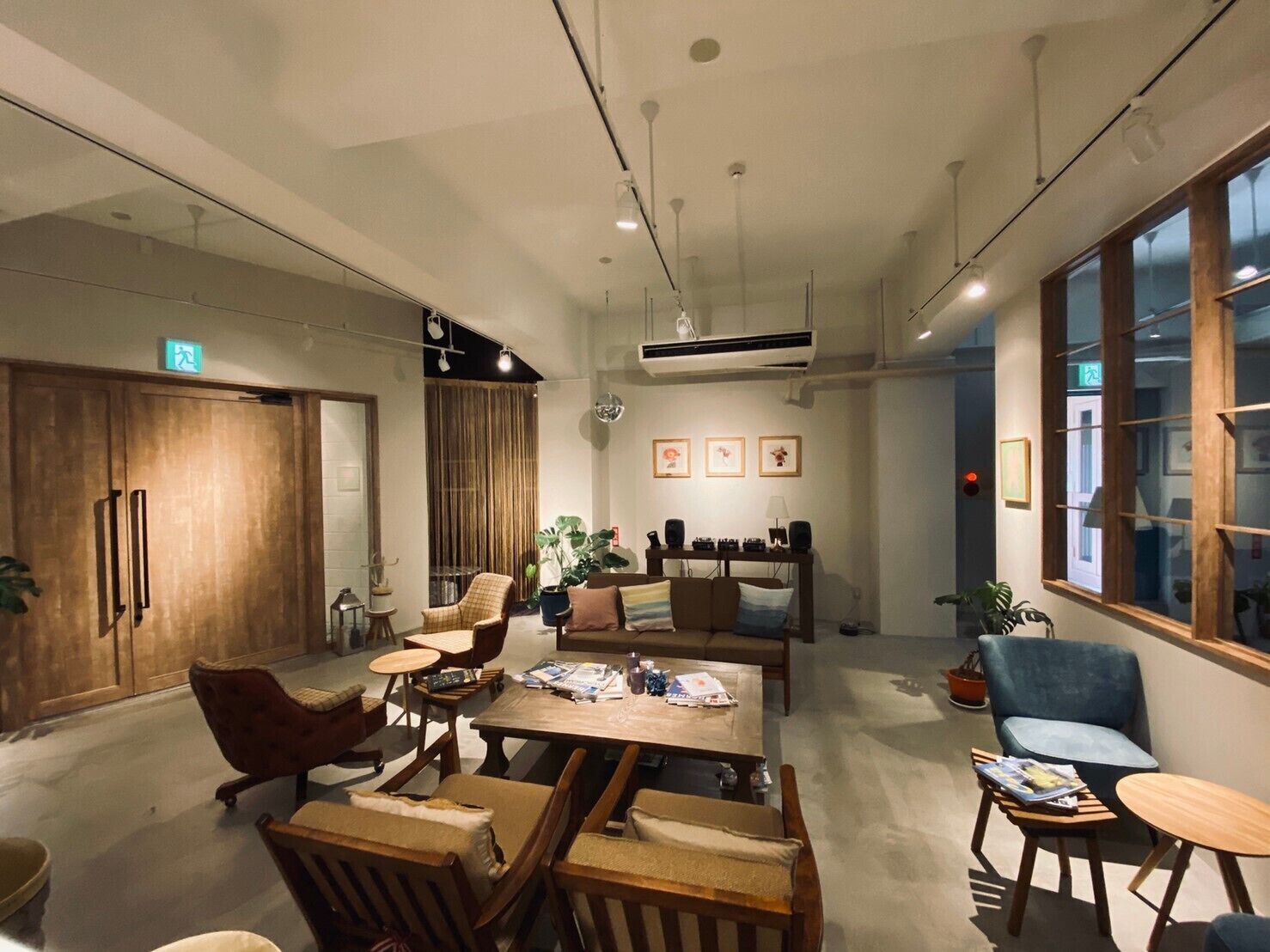 Un interior moderno con una mesa de comedor de madera, sillas y una zona de sofás. Hay plantas en macetas y cuadros en las paredes.