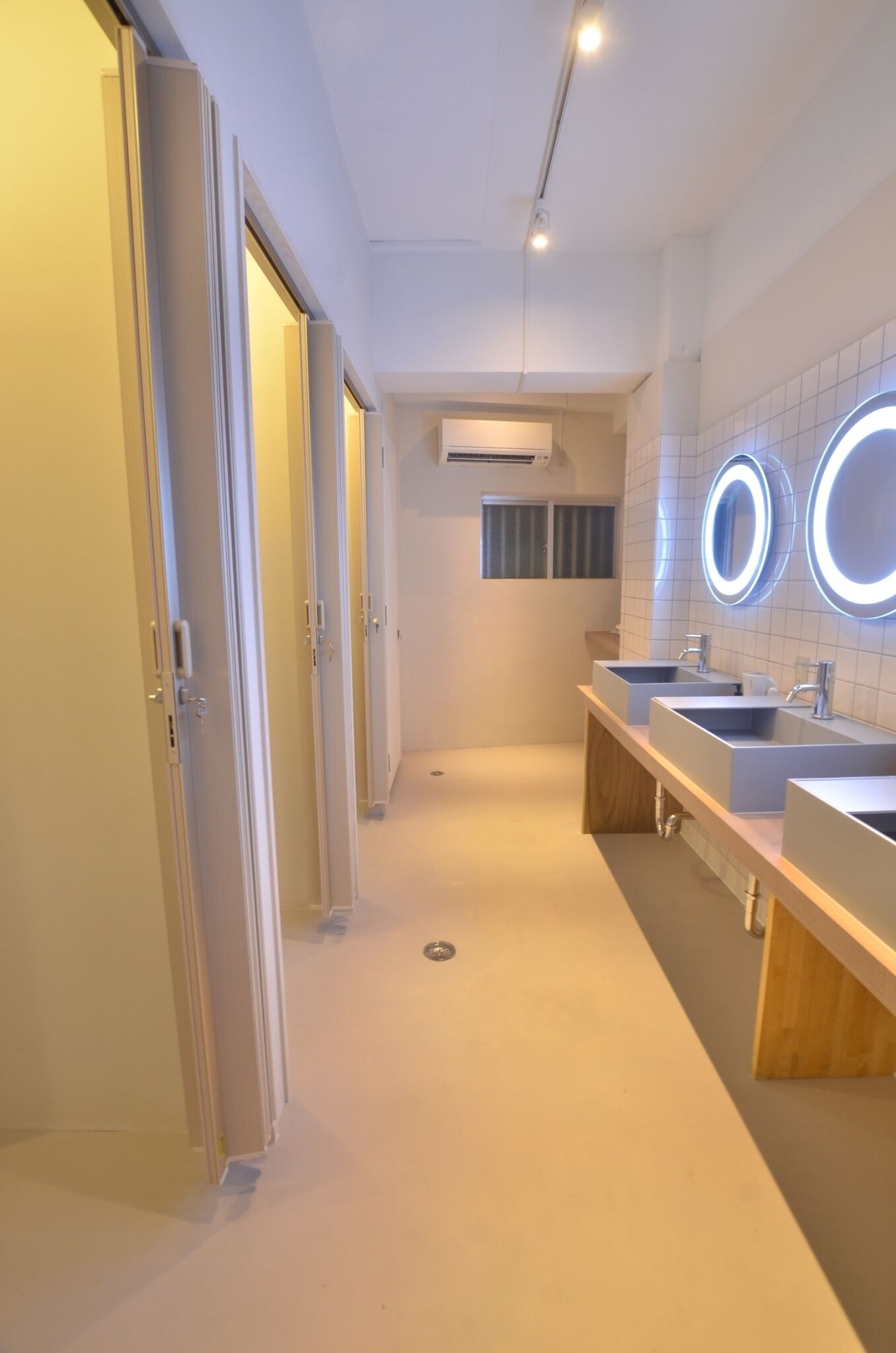 Un bany modern amb tres rentapans, un mirall amb il·luminació circular i una unitat de ventilació a la paret.
