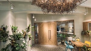 A modern interior with a wooden door, a glass wall with text, and various plants. - Lestel Naha - Hostel (Naha)