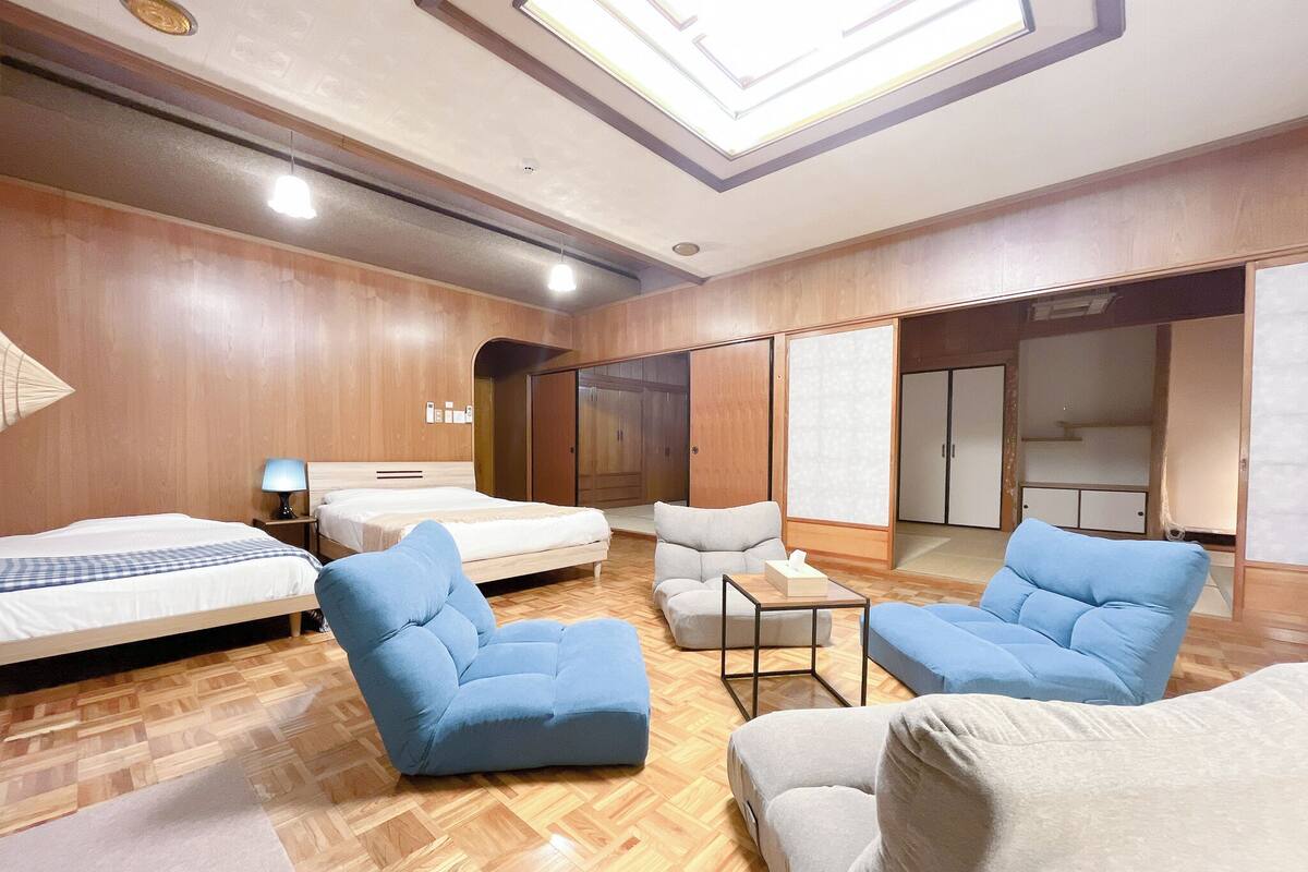 A hotel room with a bed, two blue armchairs, a small table, and a wardrobe.