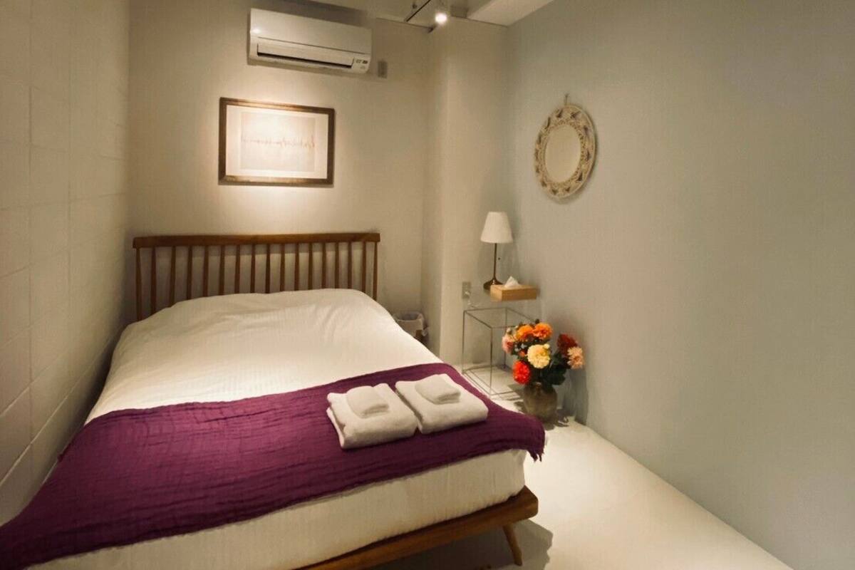 A neatly arranged bedroom with a bed, a bedside table with a lamp, and a wall-mounted air conditioner.