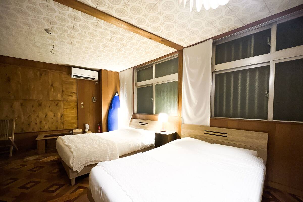 A hotel room with two beds, wooden paneling, a patterned ceiling, and a window with curtains.